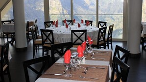 Een restaurant met gedekte tafels, met uitzicht op een berg door grote ramen.
