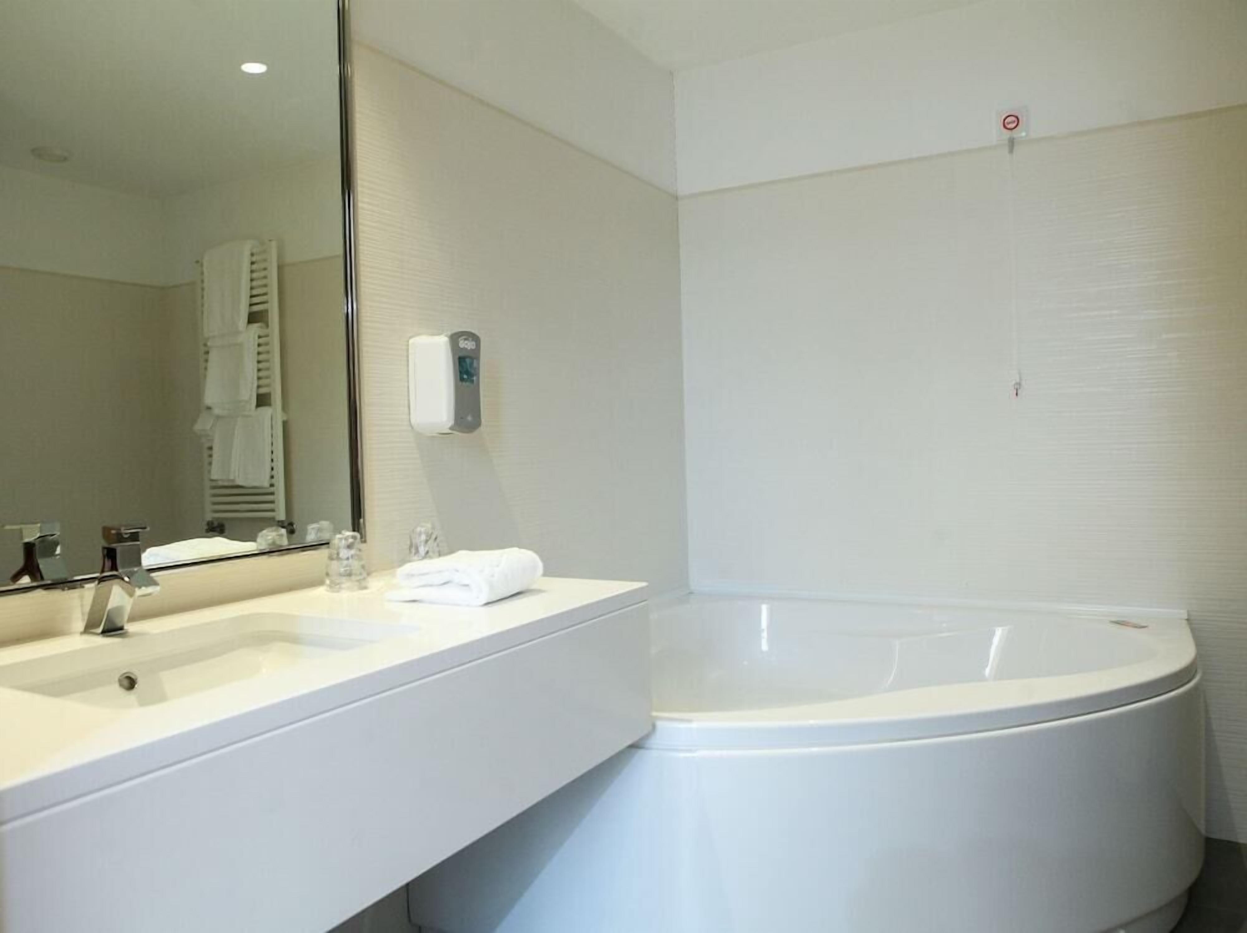 Un baño moderno con una bañera grande, un lavabo con espejo y un perchero para toallas.
