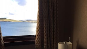 Ein Hotelzimmer mit Bett, Nachttisch, Lampe und einem Fenster mit Vorhängen.