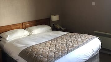 A hotel room with a large bed, a bedside lamp, a phone, and a radiator.