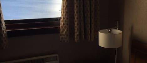 Una habitación con vistas al mar, una ventana con cortinas estampadas, una lámpara de noche y un radiador.