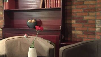Ein Zimmer mit Backsteinwand, einem Bücherregal mit Büchern, einer Vase mit einer einzelnen Blume und zwei Stühlen.