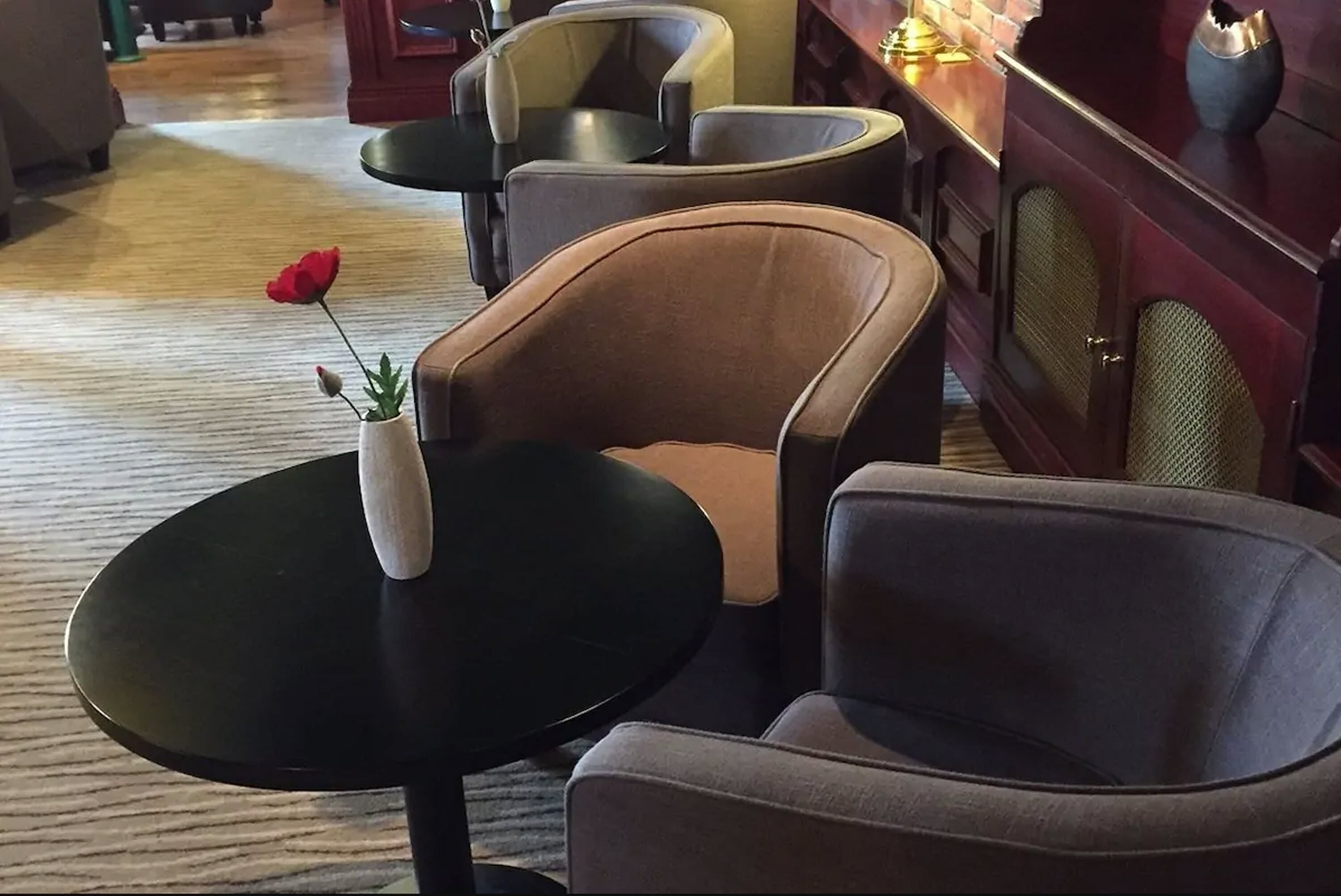 En sittgrupp med ett litet bord, en vas med en enda röd blomma och en mörkfärgad stol.