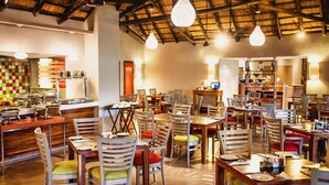 A restaurant with multiple tables and chairs, a buffet area, and a counter with food items. - Sabi River Sun (Mbombela)