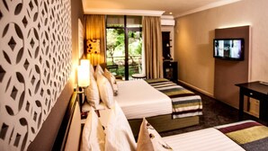 A hotel room with two beds, a TV, and a balcony with a view of greenery. - Sabi River Sun (Mbombela)