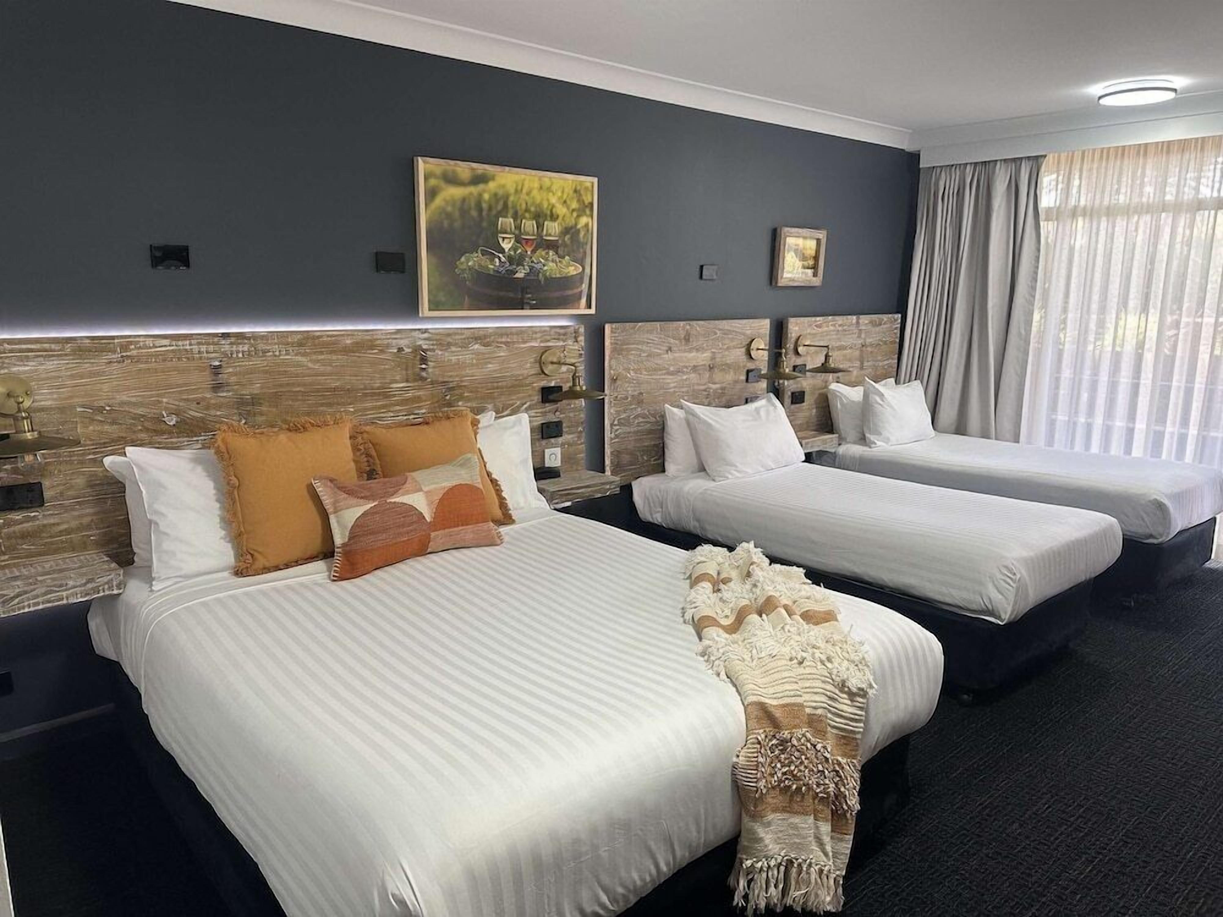 Habitación de hotel con dos camas, un cuadro grande en la pared y una ventana con cortinas.