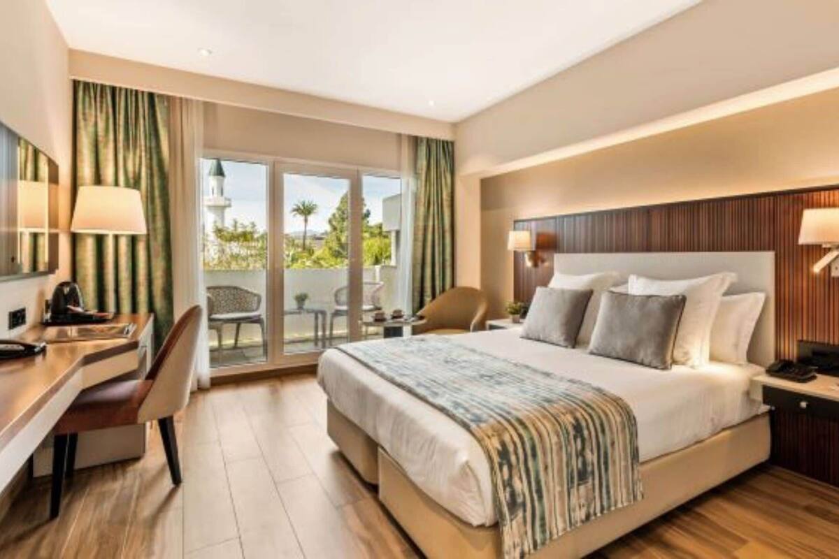 A hotel room with a bed, desk, chair, and a view of the outdoors.