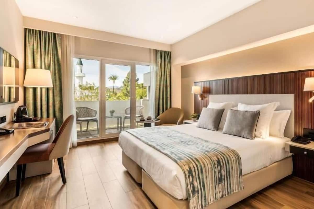 A hotel room with a bed, desk, chair, and a view of the outdoors.