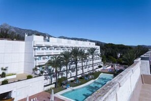 Een hotel met een zwembad, palmbomen en een berg op de achtergrond.
