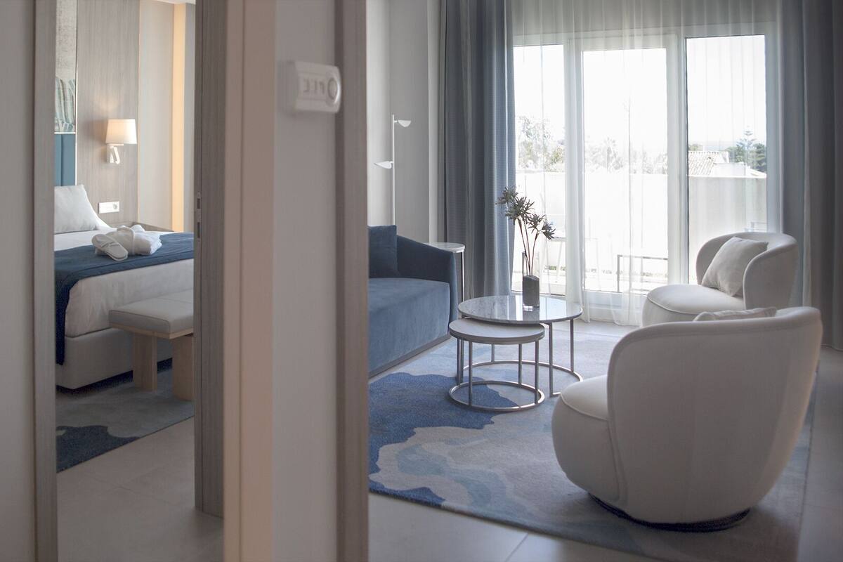 A hotel room with a bed, a sitting area with a table and chairs, and a view through the window.