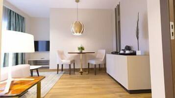 Una habitación de hotel moderna con zona de comedor, sofá, mesa y lámpara colgante.