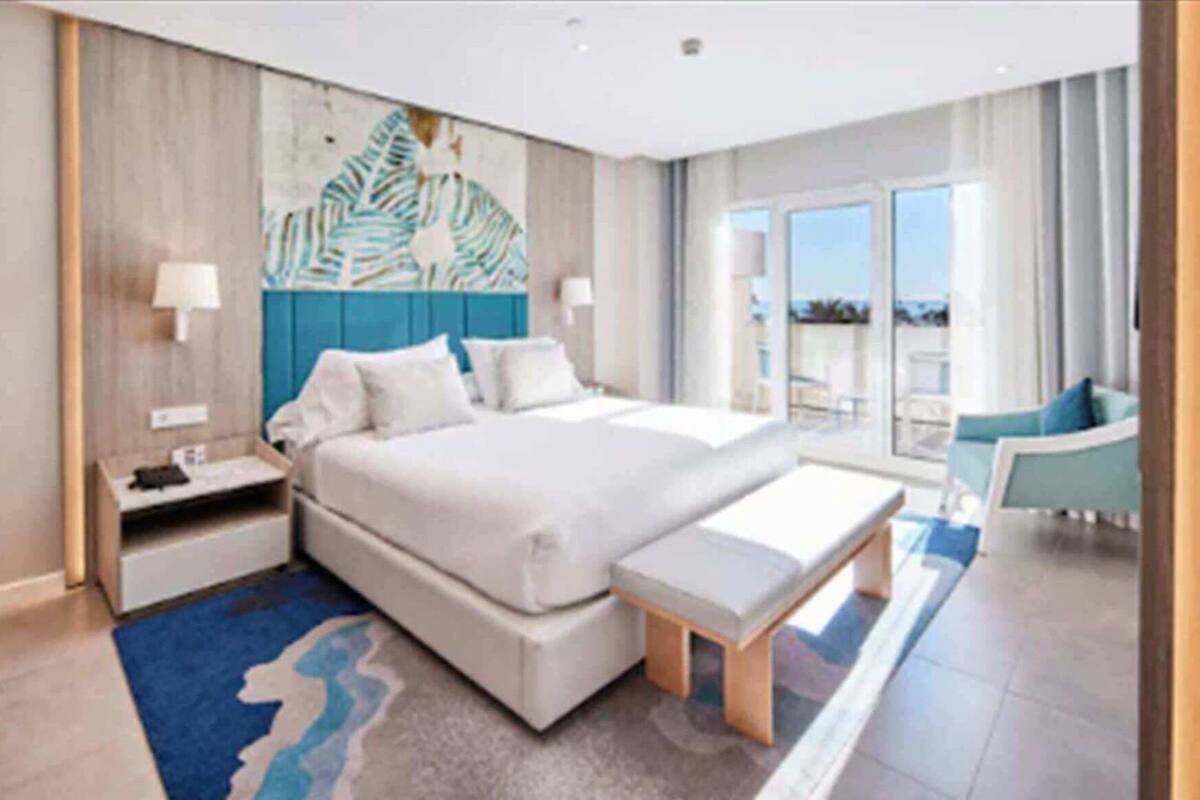 A hotel room with a large bed, a desk, a chair, and a view of the outdoors.