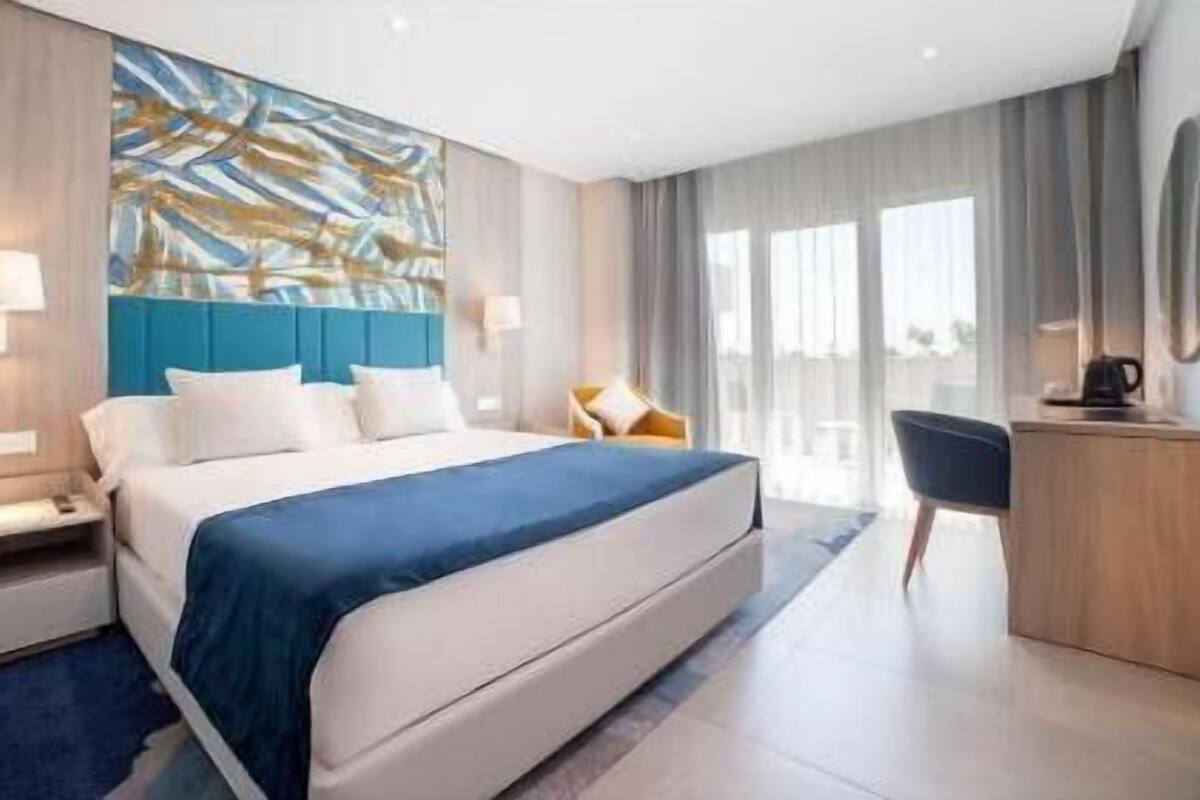 A modern hotel room with a large bed, a desk, and a view of the city.