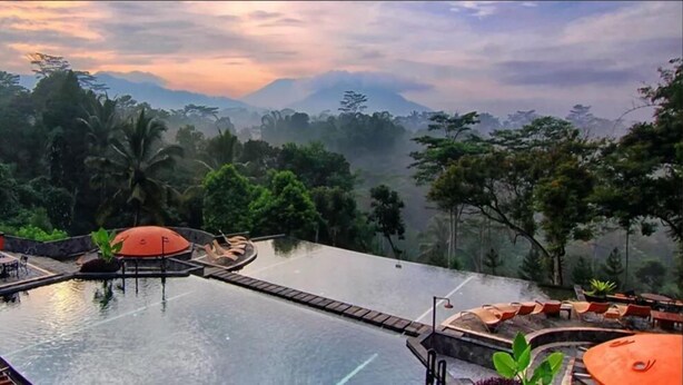 A pool area with lounge chairs and umbrellas, surrounded by lush greenery and a mountainous backdrop. - Mesastila Resort and Spa Magelang (Losari)