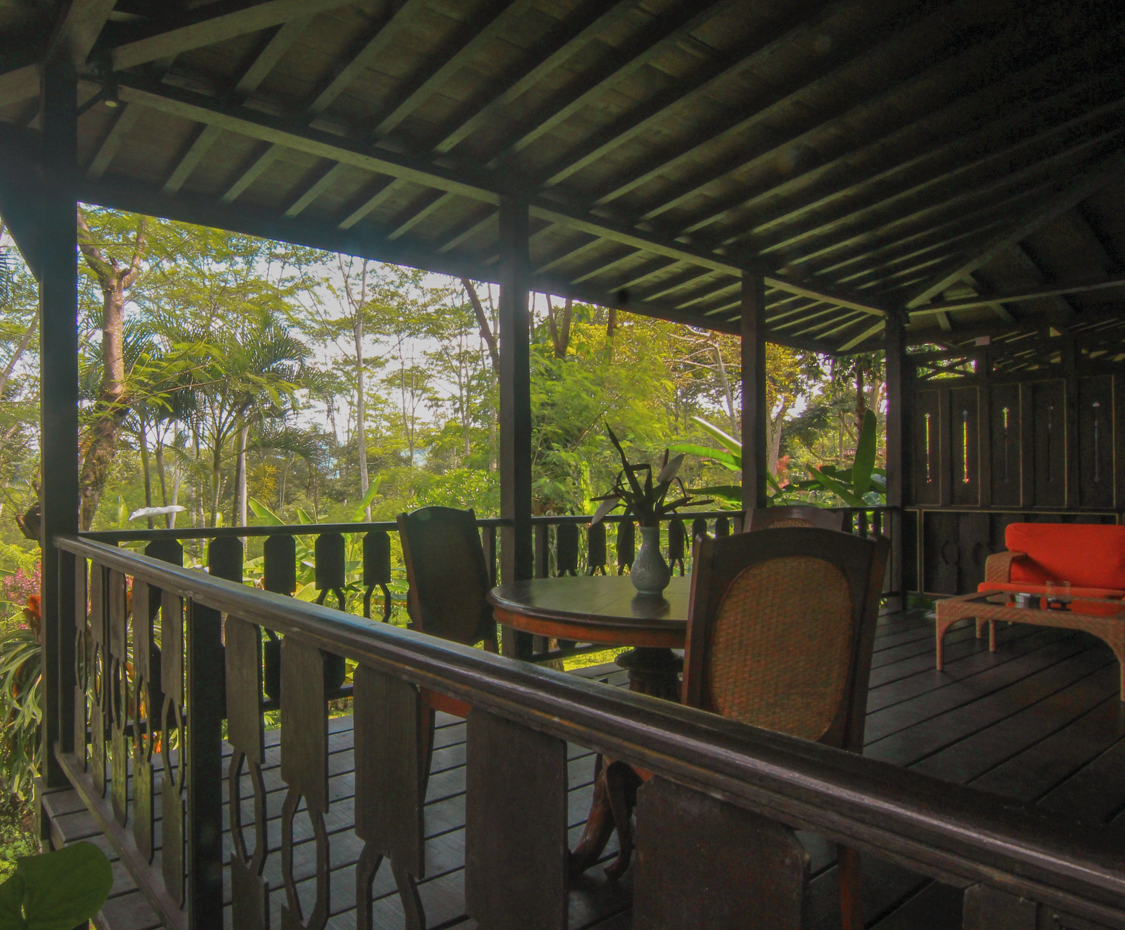 A covered outdoor area with wooden flooring, metal railings, and several chairs and tables.