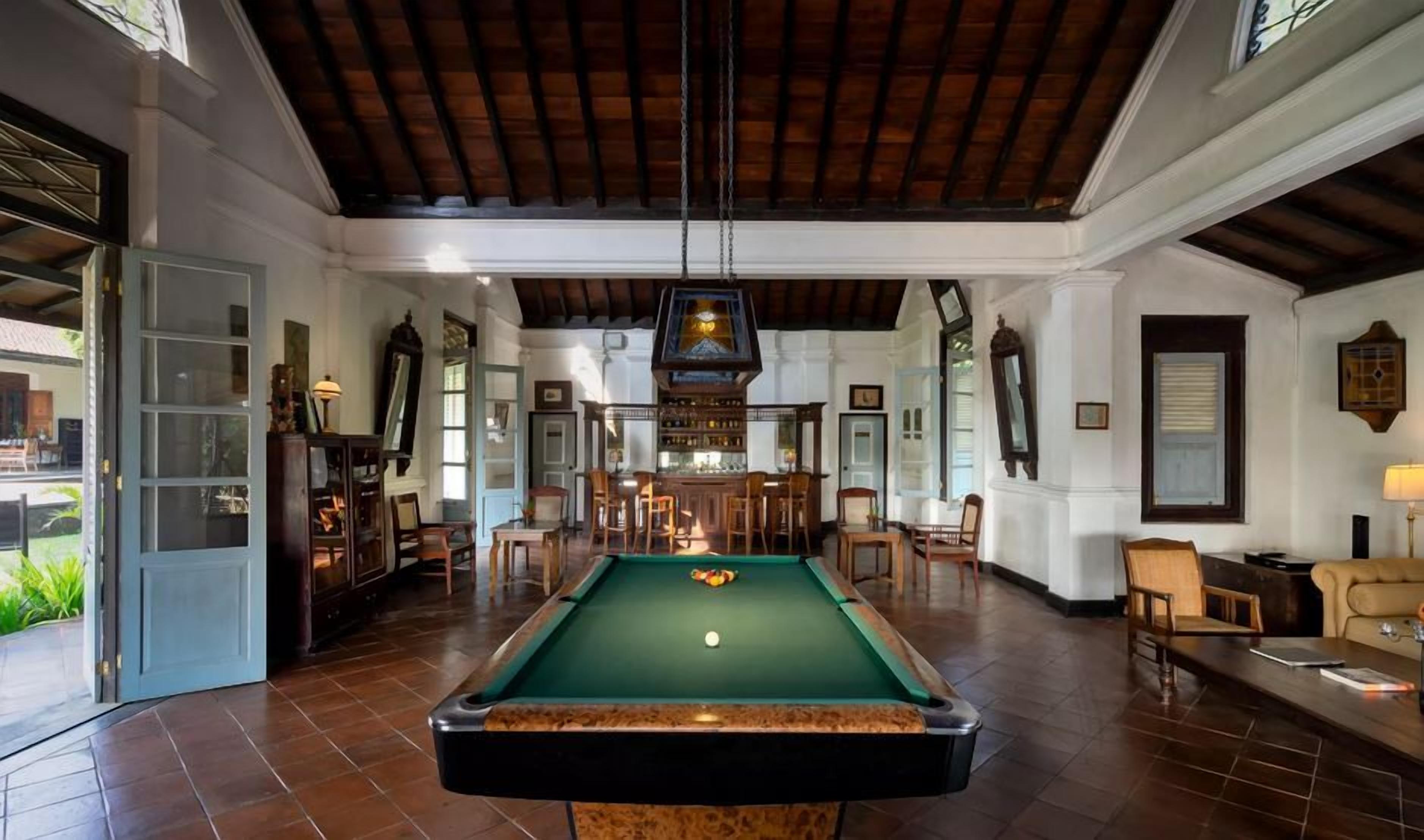 A pool table in a spacious room with a high ceiling, wooden beams, and a bar area with chairs.