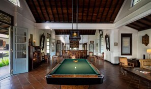 Una mesa de billar en una habitación amplia con techo alto, vigas de madera y una zona de bar con sillas.