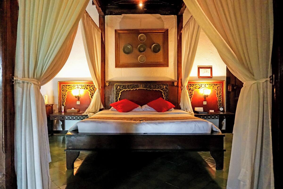 A bed with red pillows, a wooden headboard, and two bedside tables with lamps.