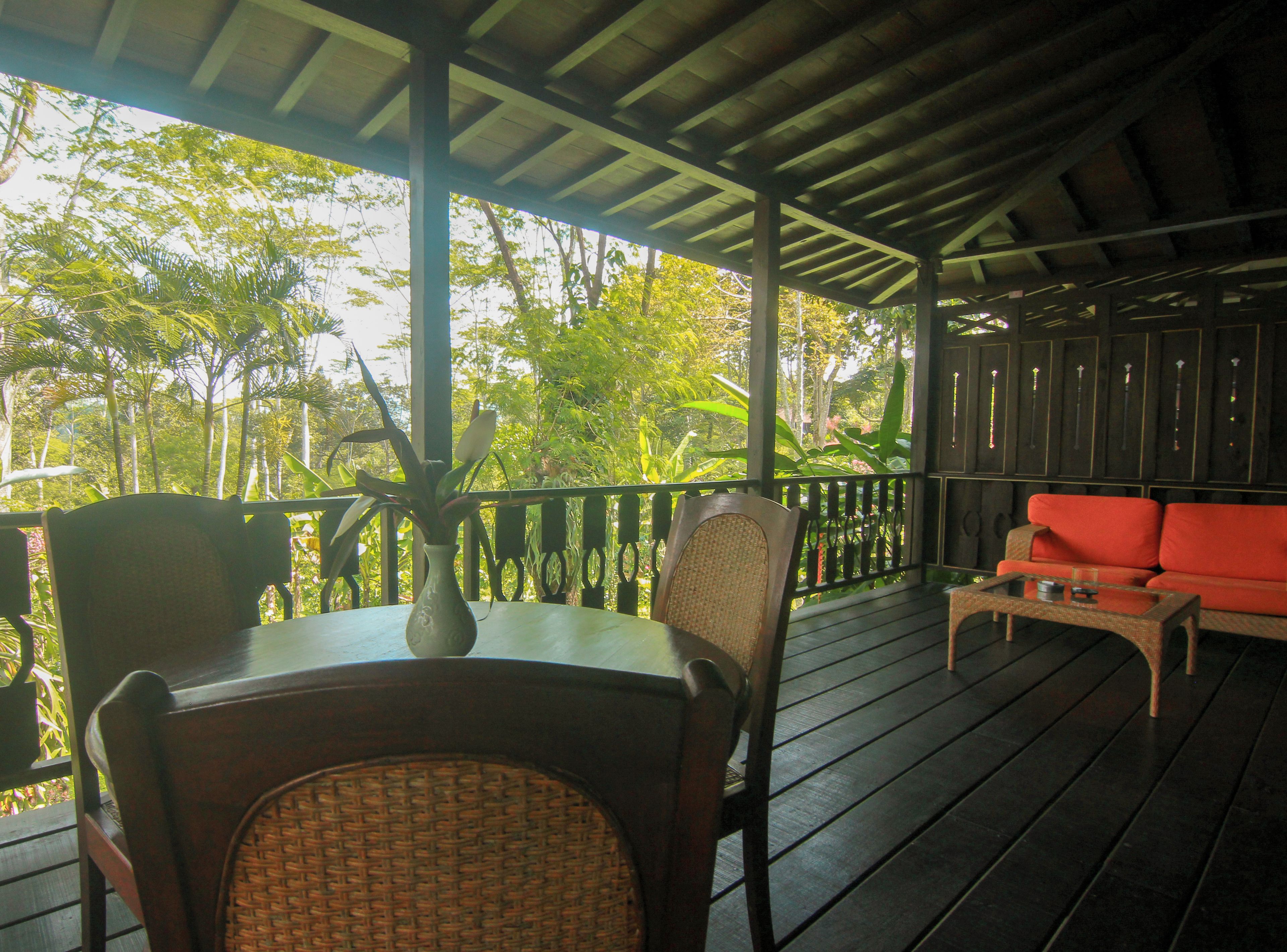 A covered outdoor seating area with a table, chairs, and a red sofa.