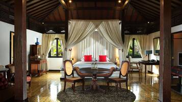 A room with a bed, a round table, and chairs, a large window, and a ceiling with wooden beams.