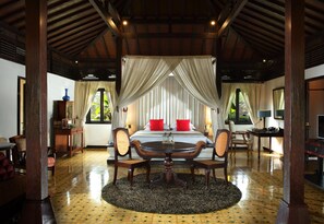 A room with a bed, a round table, and chairs, a large window, and a ceiling with wooden beams. - Mesastila Resort and Spa Magelang (Losari)