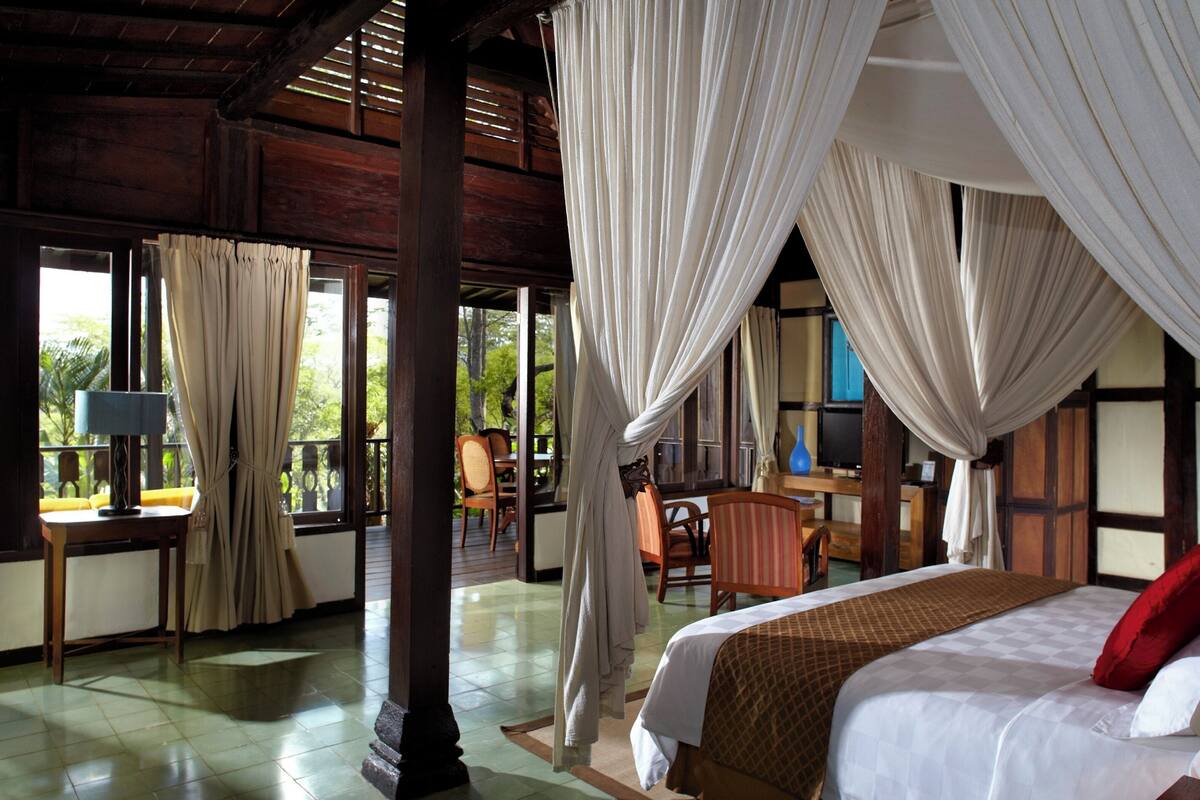 A room with a bed, a desk, and a chair. There are curtains and a window.