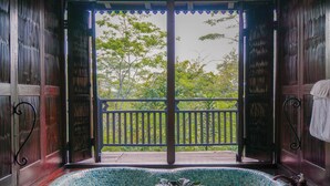 A room with a large glass door leading to a balcony, a tiled bathtub, and a potted plant. - Mesastila Resort and Spa Magelang (Losari)