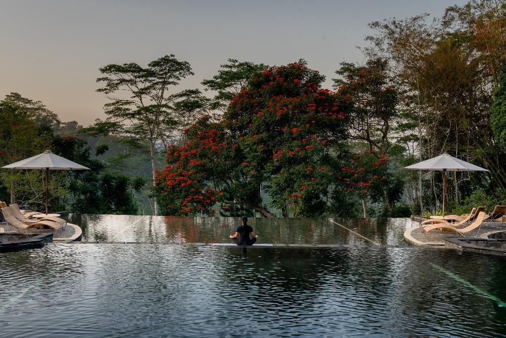 A serene outdoor pool area with lounge chairs and a person meditating.