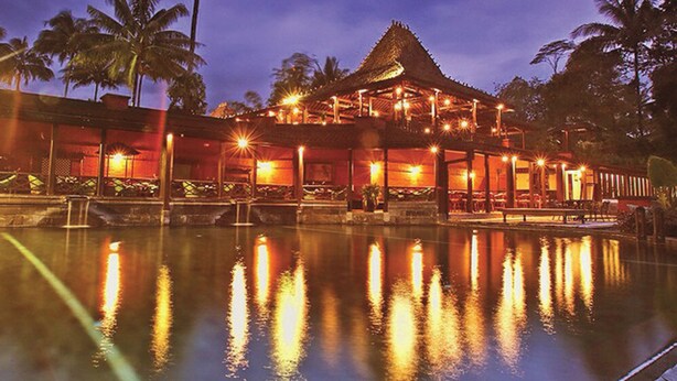 A resort with a pool reflecting lights, palm trees, and a building with a thatched roof. - Mesastila Resort and Spa Magelang (Losari)