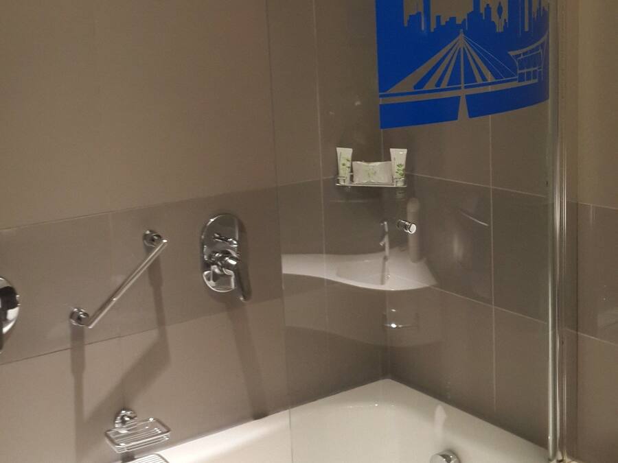 Une salle de bain moderne dotée d’une douche à parois de verre, d’une baignoire sur pieds et d’un motif décoratif représentant un paysage urbain sur le mur.