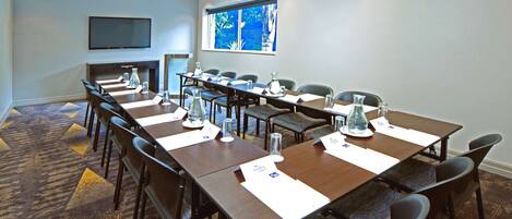 Une salle de conférence avec de longues tables, des chaises, des porte-noms et un téléviseur fixé au mur.