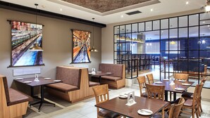 Un comedor moderno con cabinas y mesas, ventanas amplias y obras de arte en las paredes.