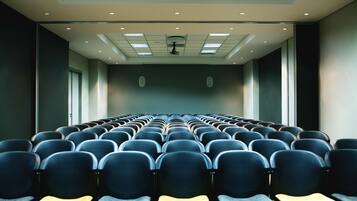 A conference room with rows of chairs, a projector screen, and ceiling lights.