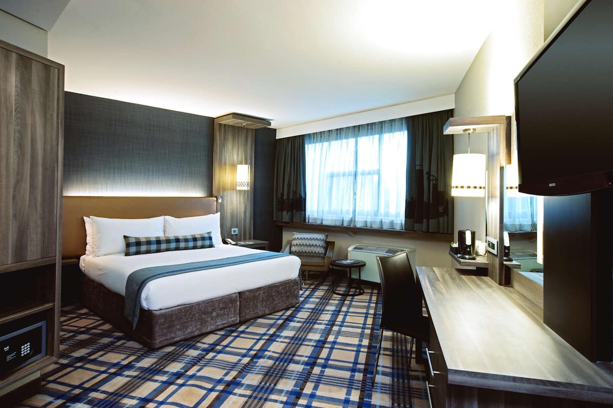 A hotel room with a large bed, a desk, a chair, a television, and a window with curtains.