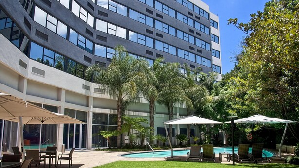 Un edificio moderno con piscina, asientos al aire libre y abundante vegetación.
