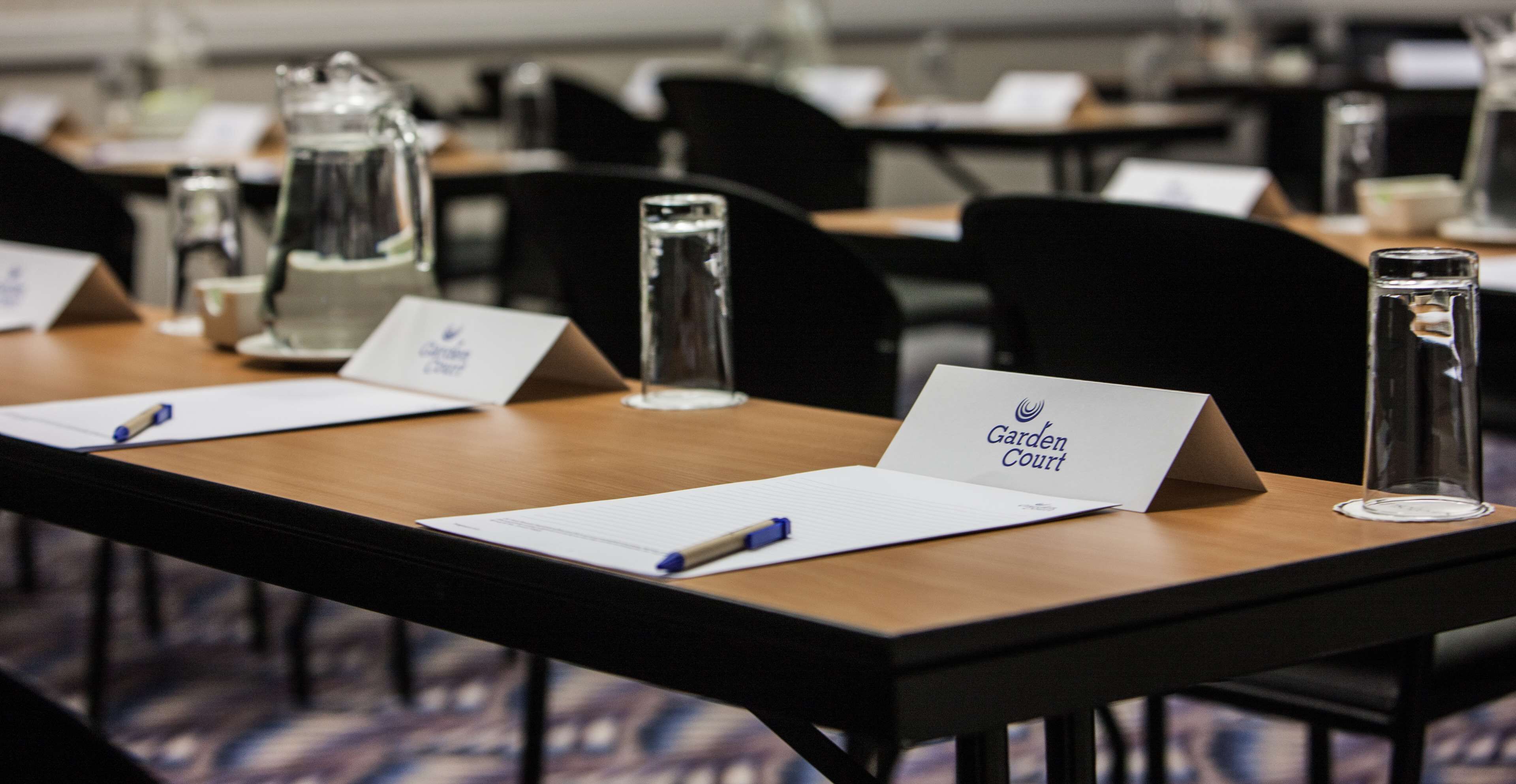 A conference room with tables equipped with nameplates, pens, and glass water bottles.