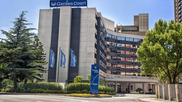 A modern building with a 'Garden Court' sign, multiple flags, and a gated entrance. - Garden Court Milpark (Johannesburg)