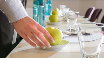 A hand placing a green apple on a white plate on a table with glasses and water bottles.