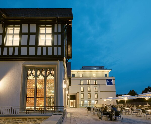 Ein Hotel mit traditioneller Bebauung und einem modernen Flügel, einem Außenbereich mit Sitzgelegenheiten und einem gut sichtbaren Eingang.