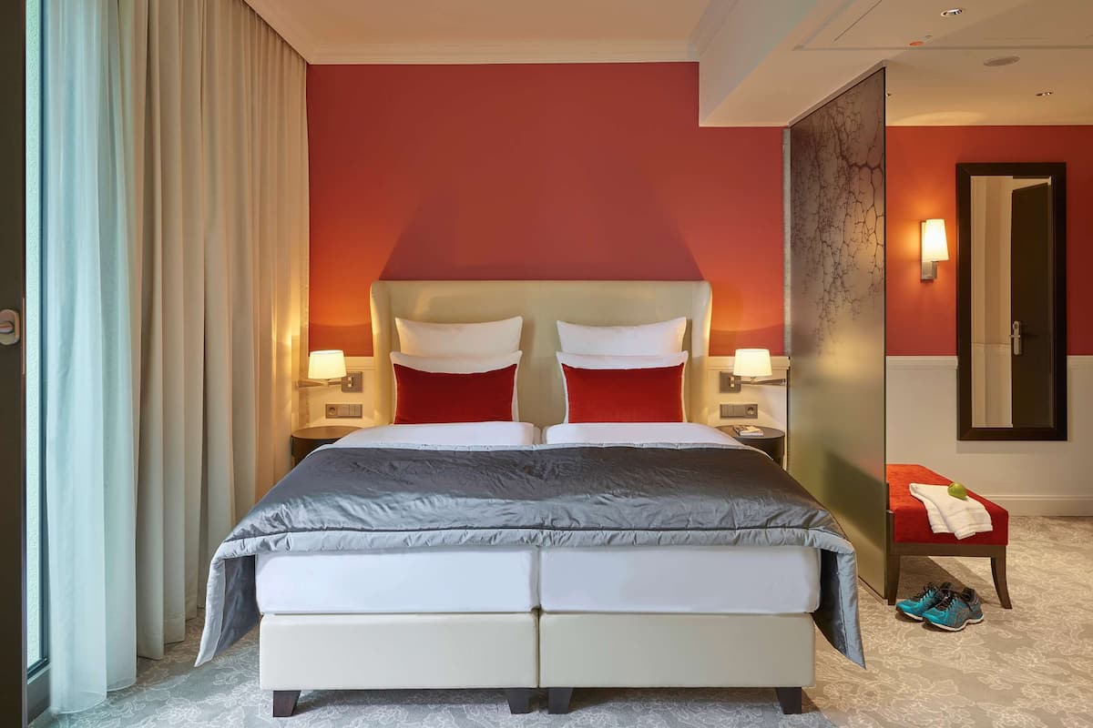 Une chambre d’hôtel avec un grand lit, deux tables de chevet avec des lampes, un mur d’accent rouge et un miroir.