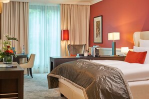 A hotel room with a large bed, a desk with a chair, a lamp, and a vase with flowers. - Dorint Hotel Frankfurt/Oberursel (Oberursel)