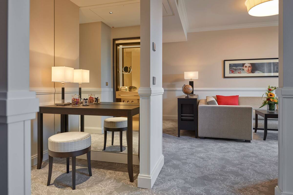 Une chambre d’hôtel moderne avec un coin repas, un canapé et une petite table agrémentée d’un globe terrestre et de fleurs.