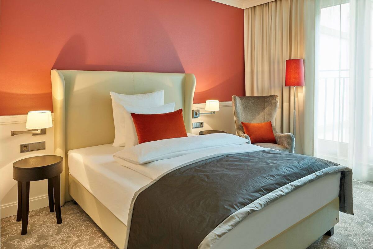 Une chambre d’hôtel avec un lit, une chaise, une table de chevet et une lampe.