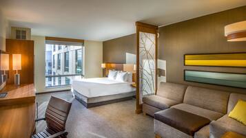 Quarto de hotel com uma cama grande, um sofá, uma escrivaninha com cadeira e janela com vista para a cidade.