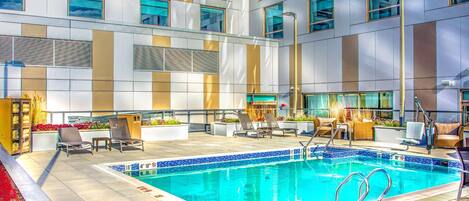 A modern indoor pool area with lounge chairs, a small pool table, and a seating area with plants.