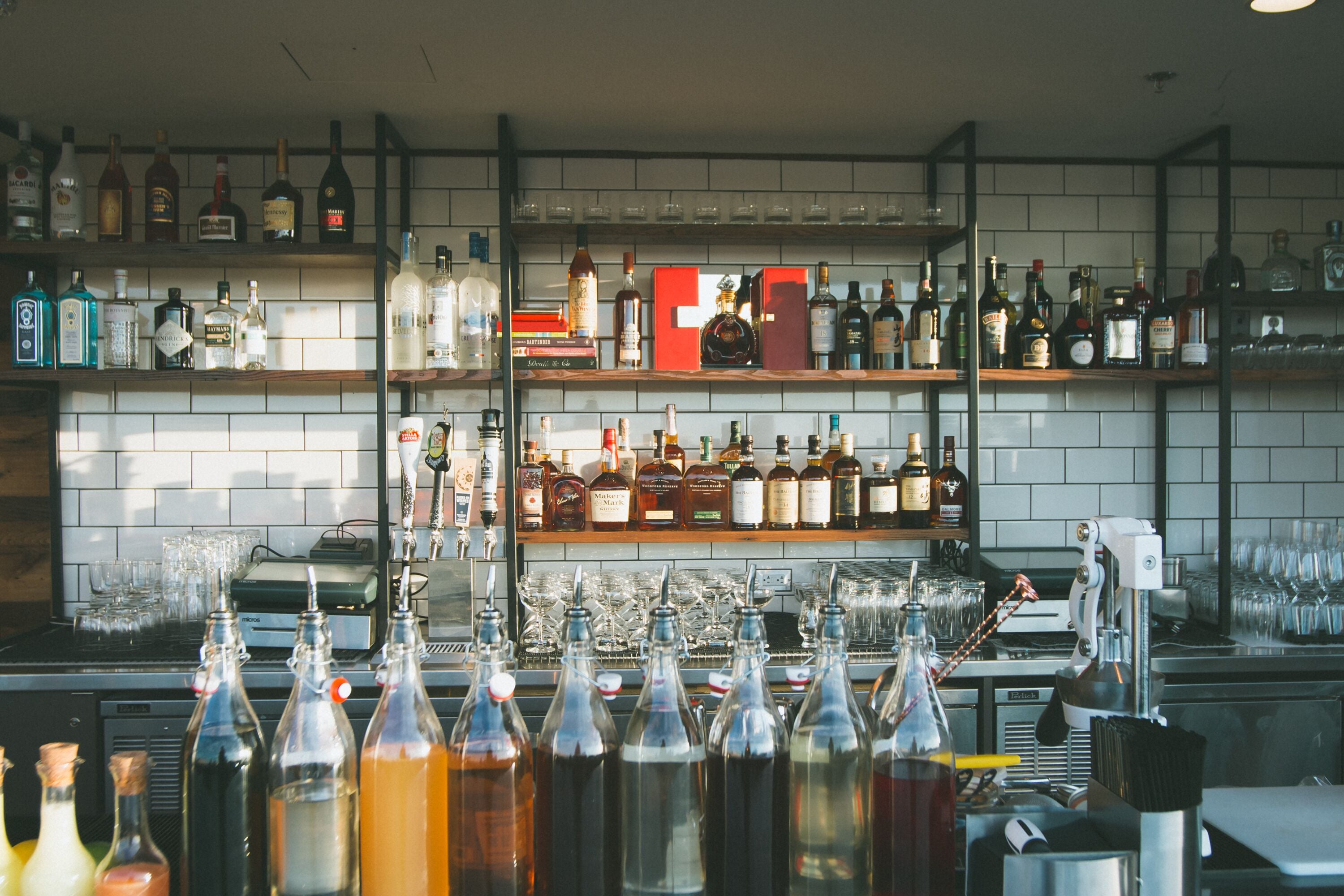 Uma área de bar com prateleiras de garrafas de bebidas, copos e uma máquina de café.