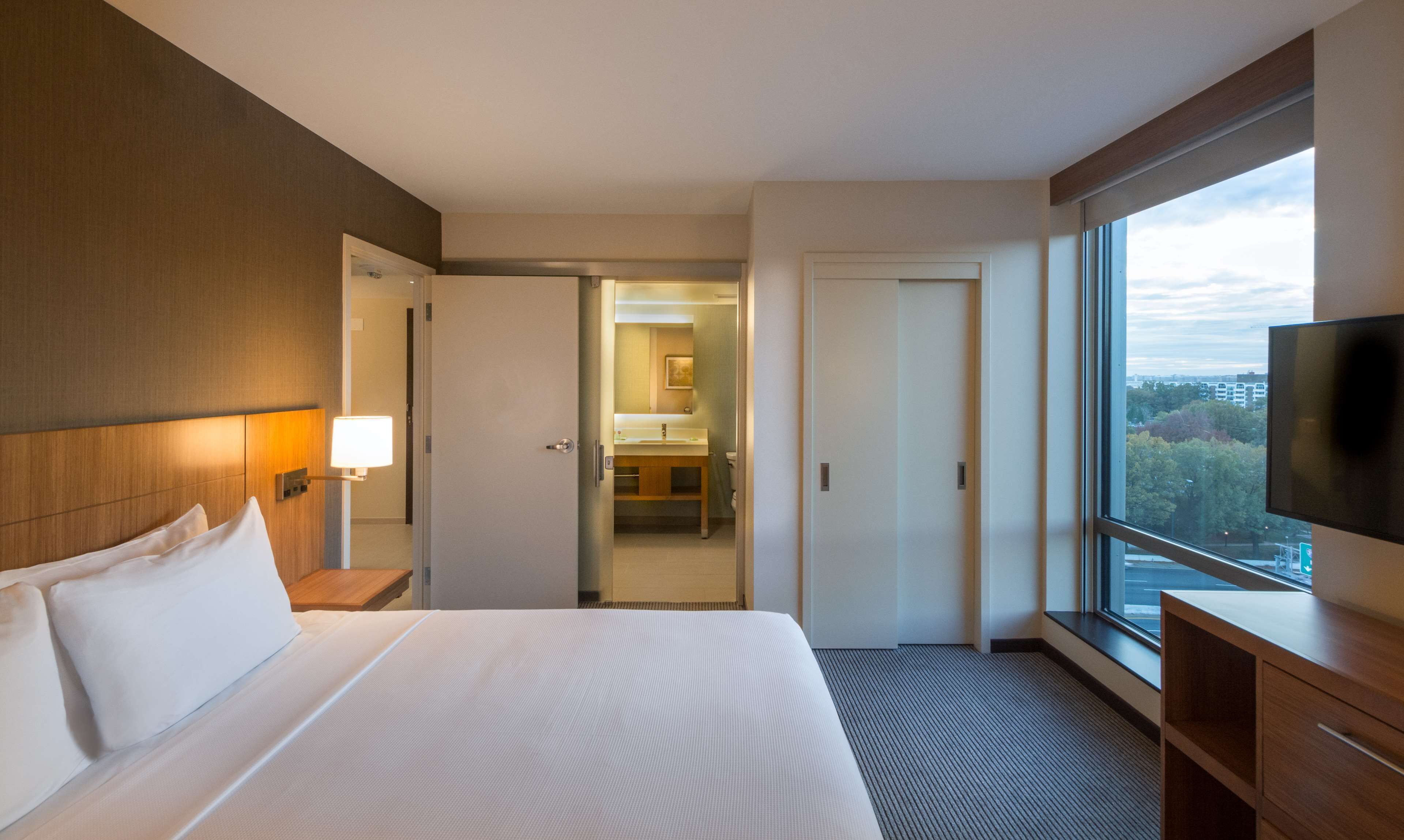 A hotel room with a large bed, a desk, a TV, and a bathroom visible through an open door.