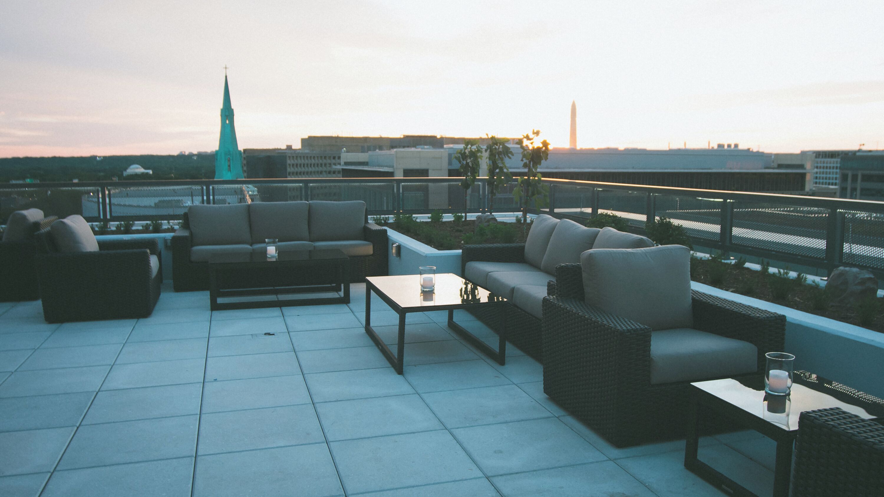 Terraza en la azotea con mobiliario exterior, incluyendo sofás y una mesa de centro, y vistas de un horizonte urbano con una aguja de iglesia.
