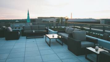 Terraza en la azotea con mobiliario exterior, incluyendo sofás y una mesa de centro, y vistas de un horizonte urbano con una aguja de iglesia.