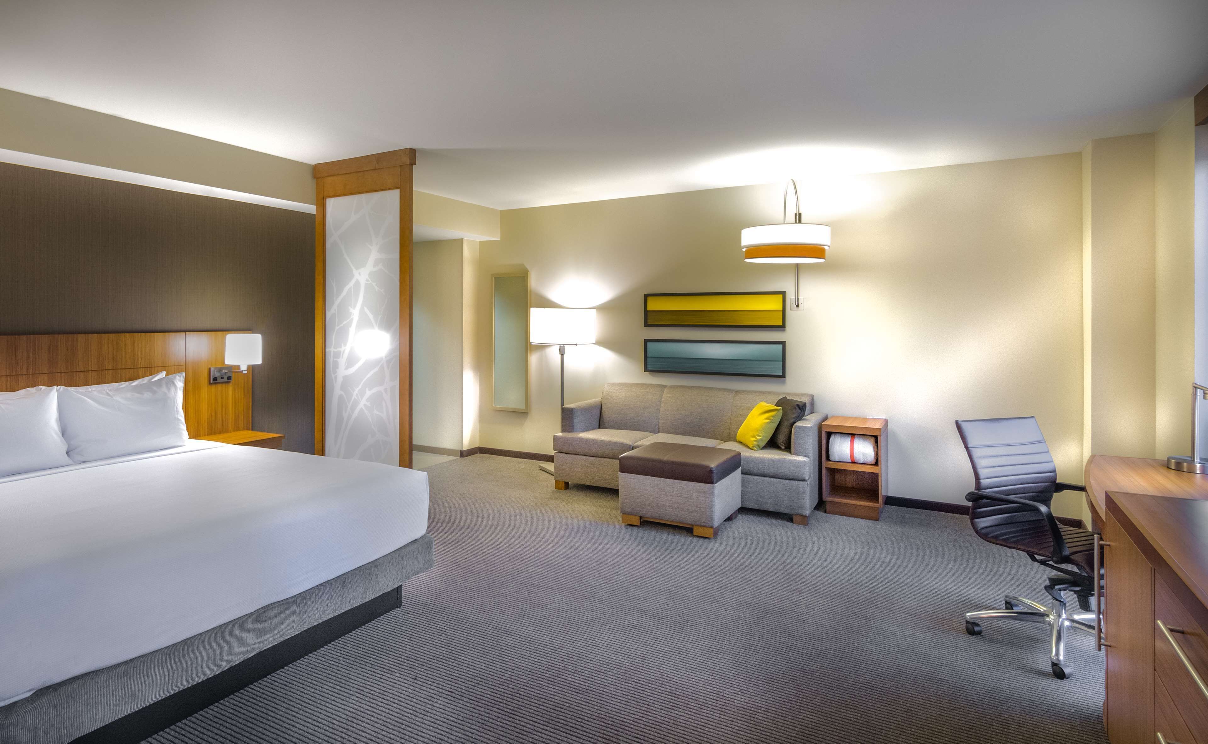 Ein Hotelzimmer mit einem großen Bett, einer Couch, einem Schreibtisch mit Stuhl und einer Lampe.
